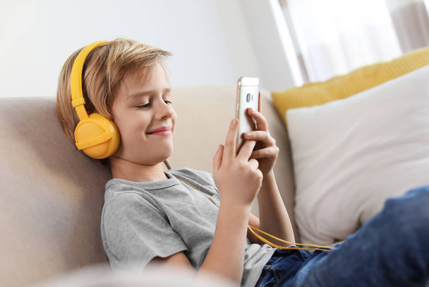 Cute little boy with headphones and smartphone listening to audiobook at home - Foto, afbeelding