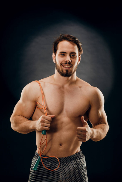 A handsome male bodybuilder with a rope in his hands on a dark background - Fotó, kép