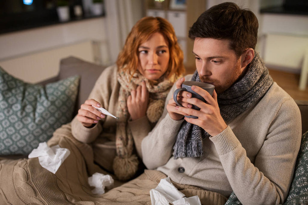 sick couple with thermometer and tea at home - Foto, Imagem