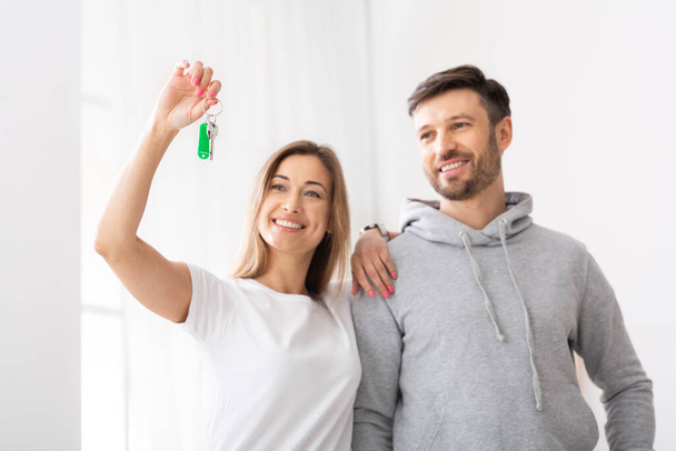 Embracing smiling couple looking at keys of new home - Foto, Bild