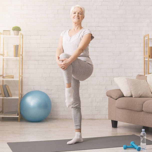 Mulher idosa alegre exercitando em casa, espaço livre
 - Foto, Imagem