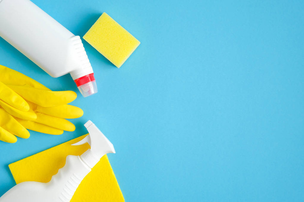 Cleaning supplies on blue background. Top view cleaner spray bottle, rag, yellow sponge, detergent, rubber gloves. House cleaning service and housekeeping concept - 写真・画像