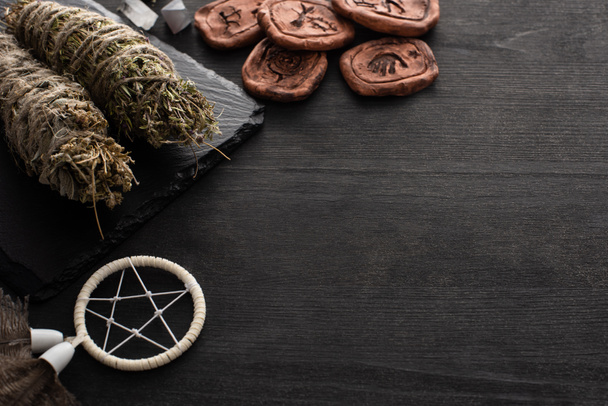 Palitos de mancha de ervas, dreamcatcher e amuletos de argila no fundo de madeira escura
 - Foto, Imagem