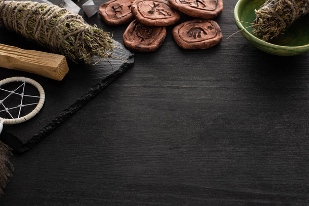 Amuletos de barro perto de varas de mancha xamânicas e apanhador de sonhos na superfície de madeira escura
 - Foto, Imagem