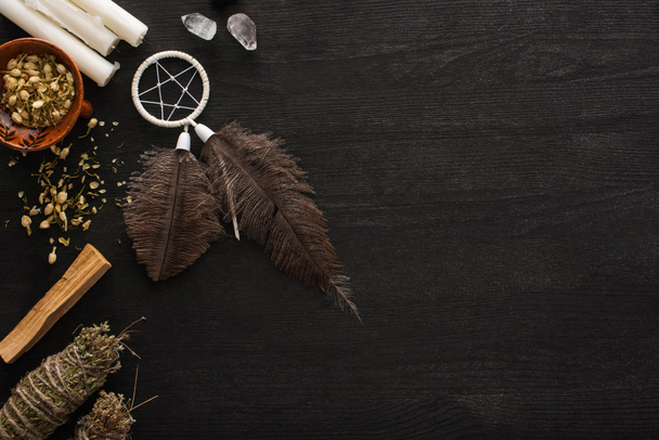 Top view of dreamcatcher, smudge sticks with magical crystals and candles on dark wooden surface - Photo, Image