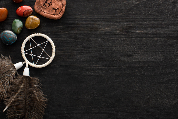 Top view of dreamcatcher, fortune telling stones and magic rune on dark wooden background - Fotó, kép