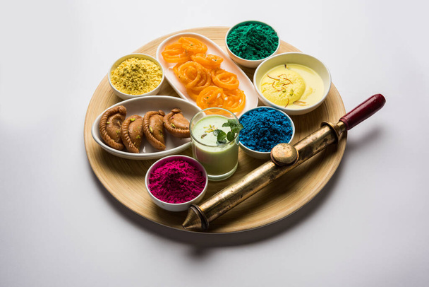 Happy Holy concepto mostrando dulces indio surtidos como jalebi, gujiya, que, ras malai con colores holi y pichkari, aislado sobre fondo blanco
 - Foto, Imagen