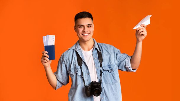 Cheerful guy with camera holding passport and paper airplane - Photo, Image