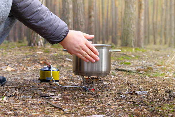 Camper is cooking dinner in a metal pan during camping. Enjoy a tasty food during hiking trips. Tourist food on a gas burner for outdoor activities. - Photo, Image