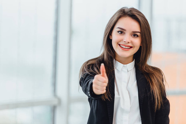 Closeup portrait of pretty office employee showing thumb up isolated near window. - Photo, Image