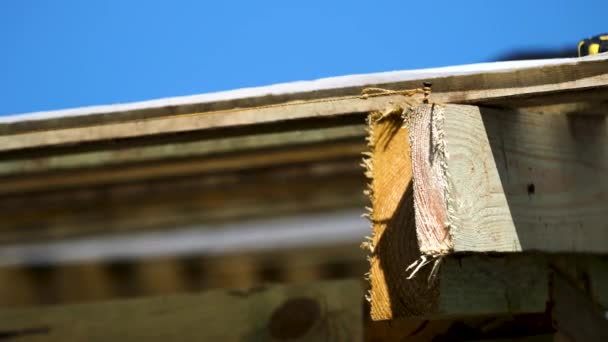 Close up of roofing wooden construction with a nail and a tight rope around it on blue sky background. Stock footage. Rough wooden boards and roof covering white cloth swaying in the wind. - Πλάνα, βίντεο
