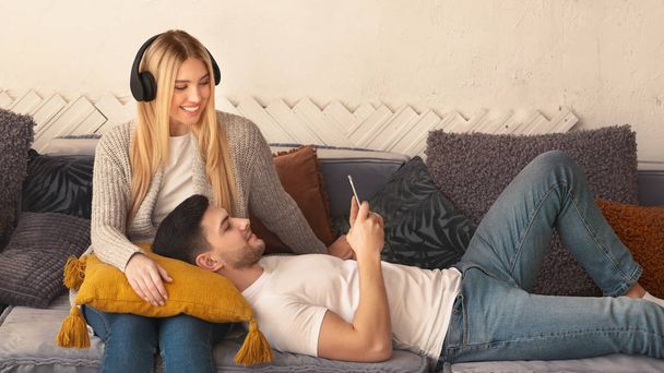 Αγαπημένο ζευγάρι με ακουστικά και κινητό τηλέφωνο στον καναπέ στο σπίτι - Φωτογραφία, εικόνα