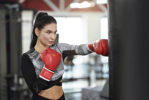 Cours d'autodéfense. Jeune femme en gants de boxe punching ball dans la salle de gym
 - Photo, image