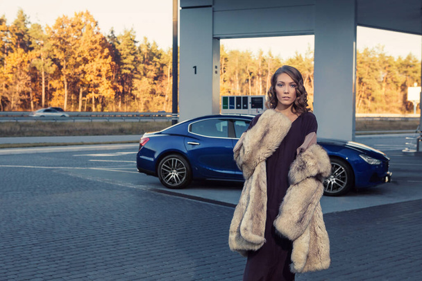 The elegant blonde beautiful woman posing near luxury vehicle. Beautiful young woman with blue luxury car. Sexy female enjoying trip on luxury modern car. Fashionable lifestyle concept. - Foto, afbeelding
