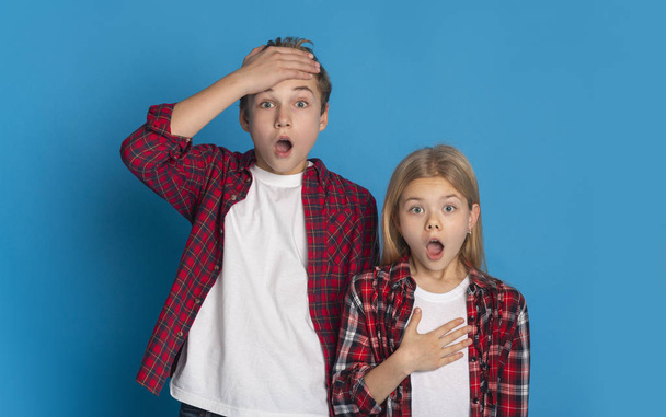 Shocked brother and sister standing with opened mouth over blue background - Photo, Image