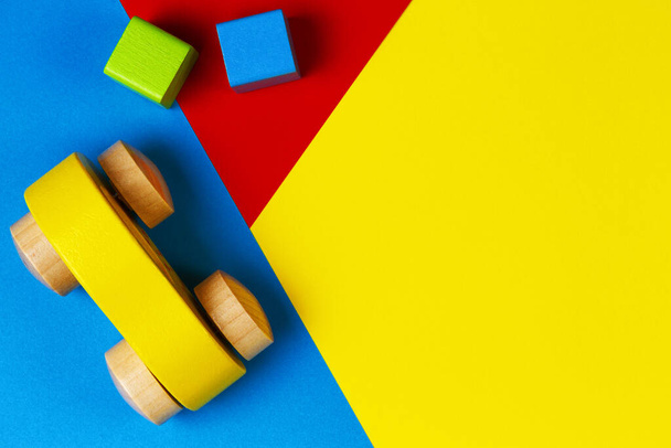 Coche de juguete rojo de madera con bloques de colores sobre fondo verde azul amarillo geométrico. Vista superior
 - Foto, Imagen