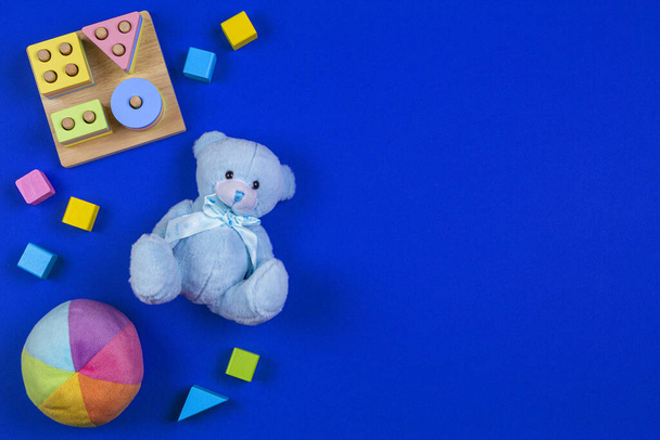 Dzieciaki w tle zabawki. Niebieski miś, kolorowe klocki drewniane, kształt rozpoznawania kolorów układarka na granatowym tle. Widok z góry - Zdjęcie, obraz