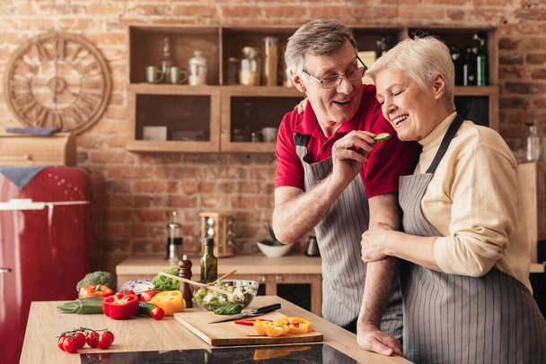 Amare l'uomo anziano nutrire sua moglie con cetriolo in cucina
 - Foto, immagini