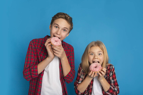Dolci malsani. Preteen fratello e sorella mangiare ciambelle su sfondo blu
 - Foto, immagini