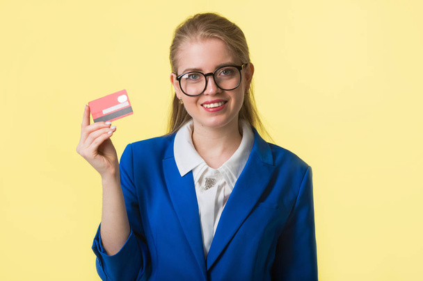 bela jovem mulher em uma jaqueta azul em um fundo amarelo com um cartão de crédito em suas mãos
 - Foto, Imagem