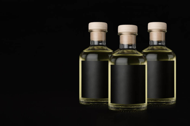 Three glass bottles for cosmetic, perfume, drink with black label, cork, yellow liquid on black background, mock up for design product, copy space. - Foto, immagini