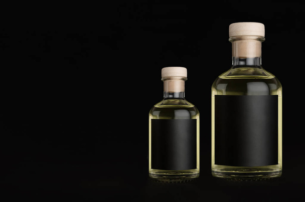 Big and small glass bottles for cosmetic, perfume, drink with black label, cork, yellow liquid on black background, mock up for design of product. - Photo, image