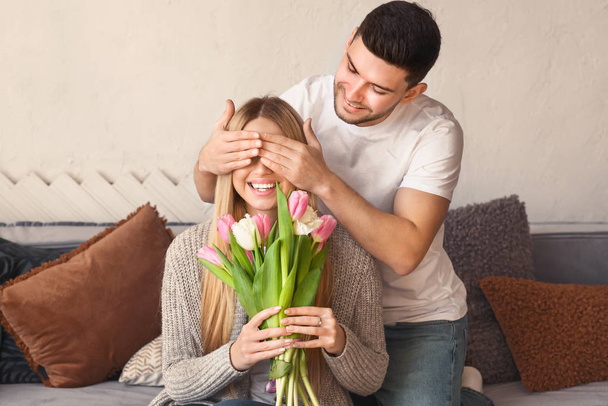 Sevecen genç bir adam evde çiçeklerle sevgilisine sürpriz yapıyor. - Fotoğraf, Görsel