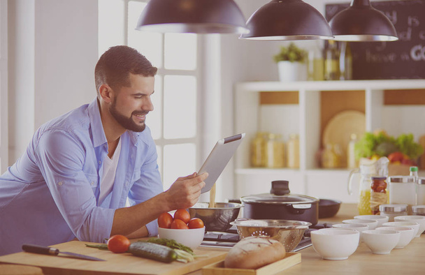 Mann folgt Rezept auf digitalem Tablet und kocht leckeres und gesundes Essen in der heimischen Küche - Foto, Bild