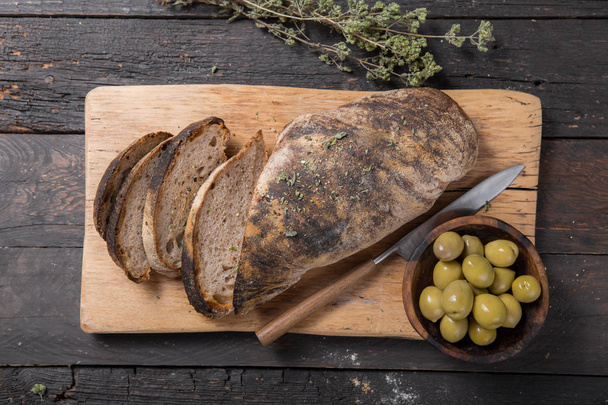 Pão de ciabatta italiano fresco para fermento com ervas, azeitonas em fundo de madeira, vista superior, espaço de cópia
. - Foto, Imagem