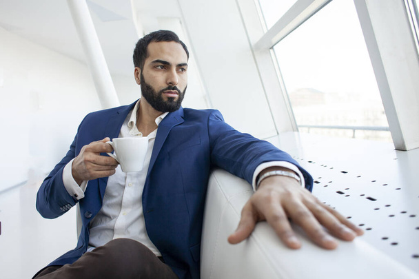schöner erfolgreicher Geschäftsmann im Anzug sitzt in einem Café, trinkt Kaffee und schaut aus dem Fenster, kopiert Raum - Foto, Bild