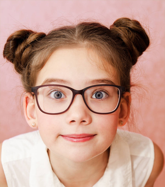 Portrait of funny smiling little girl child wearing glasses isolated on a pink background - Zdjęcie, obraz