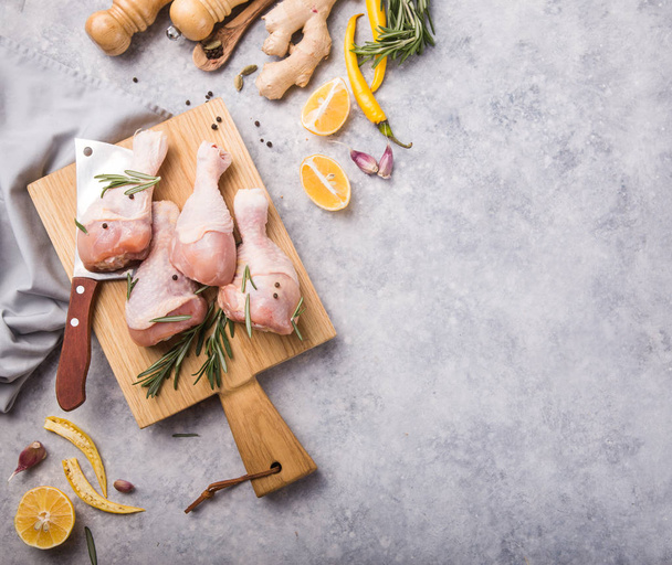 Raw organic uncooked chicken legs or drumsticks on cutting board  with ingredients for cooking (pepper, lemon, rosemary, salt, garlic). Meat top view - Photo, Image
