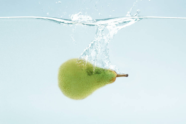 Saftige Birne fliegt ins Wasser mit Spritzer auf blauem Hintergrund - Foto, Bild