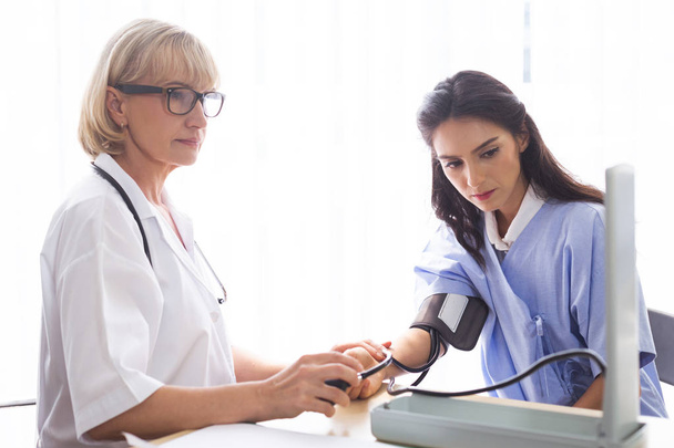 Vrouwelijke artsen meten de patiëntendruk in de onderzoekskamer van het ziekenhuis.. - Foto, afbeelding