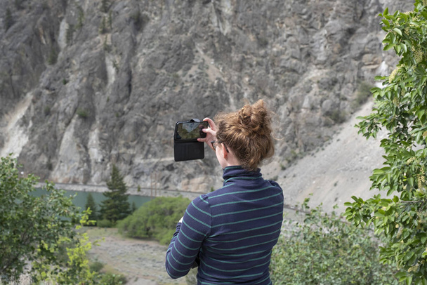Die junge Frau fotografiert mit ihrem Handy einen See, sie trägt lässige Kleidung. Wells Gray Provinzpark, British Columbia, Kanada - Foto, Bild