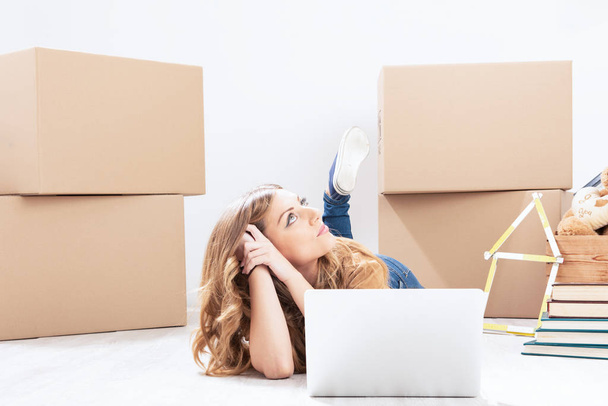 Молодая блондинка ремонтирует свой дом, сидя на полу в окружении картонных упаковочных картонных коробок с помощью планшета-p - Фото, изображение