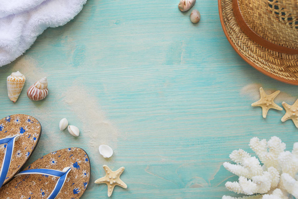 Sea shells, starfishes, coral; terry towel; slippers and straw hat as frame on the background of  blue faded wooden deck. Marine holidays concept - Фото, зображення