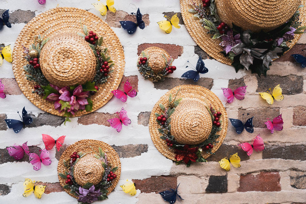 Fedora Sommer Sonnenhut und bunte getrocknete Blumen Arrangement und Schmetterlinge Dekoration hängen an einer Ziegelwand. - Foto, Bild