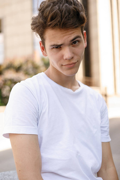 Elegant young man smile in a fashionable black shirt in a white stylish t-shirt in black pants with a trendy hairstyle rests near a modern business center. close-up portrait - Foto, immagini