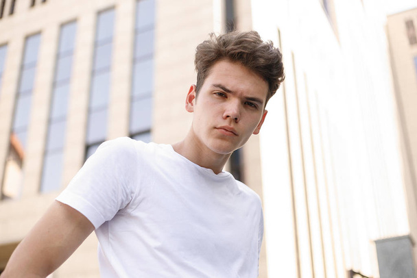 Elegant young man smile in a fashionable black shirt in a white stylish t-shirt in black pants with a trendy hairstyle rests near a modern business center. close-up portrait - Fotografie, Obrázek