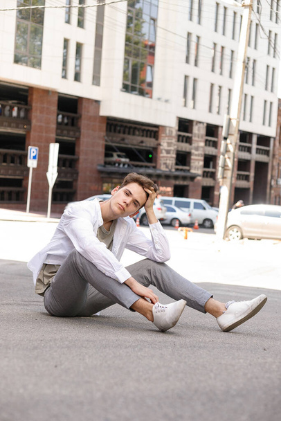 guy model with a stylish haircut posing outdoors in a white shirt and gray trousers. trendy hairstyle rests near a modern business center. Attractive guy in the street on a summer day. - Φωτογραφία, εικόνα