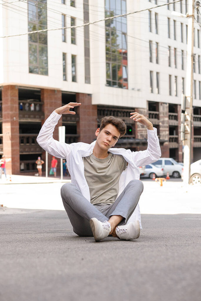 guy model with a stylish haircut posing outdoors in a white shirt and gray trousers. trendy hairstyle rests near a modern business center. Attractive guy in the street on a summer day. - Photo, image