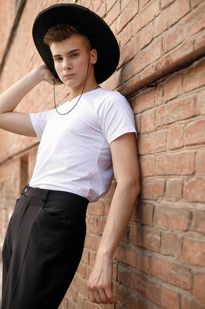 portrait of a trendy young man in the city. close-up portrait guy model in a black hat a brick wall background - Photo, Image