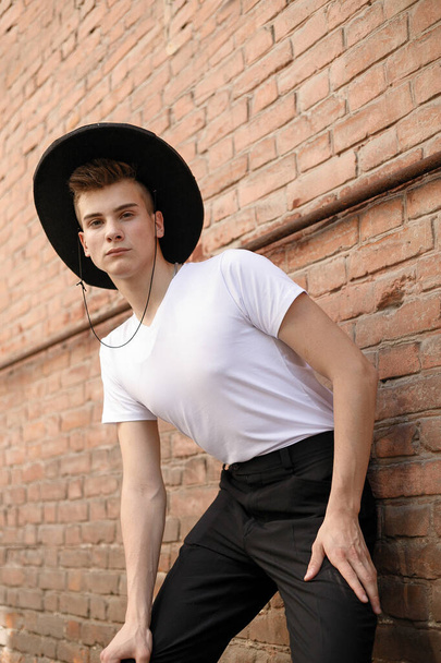 portrait of a trendy young man in the city. close-up portrait guy model in a black hat a brick wall background - Fotoğraf, Görsel