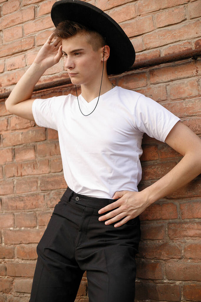 portrait of a trendy young man in the city. close-up portrait guy model in a black hat a brick wall background - Φωτογραφία, εικόνα