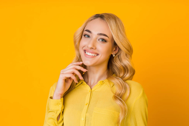 Cheerful girl touching chin and smiling, yellow background - Foto, afbeelding
