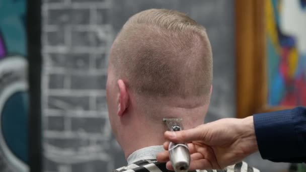 Mens haircut in Barbershop. Close-up of master clipping a man with blond hair with clipper - Materiał filmowy, wideo