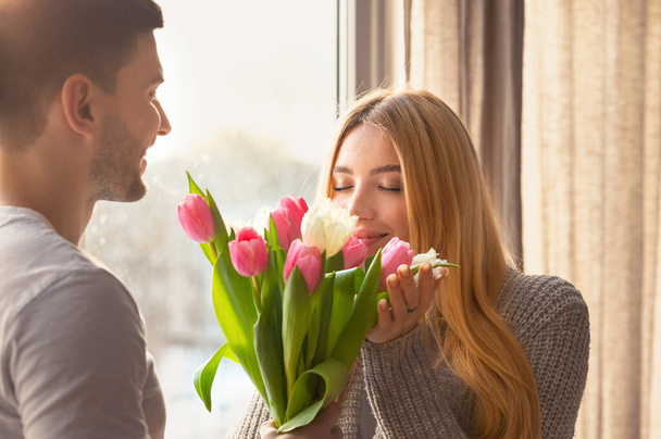 Liefdevolle jongeman presenteert boeket bloemen aan zijn vrouw thuis - Foto, afbeelding