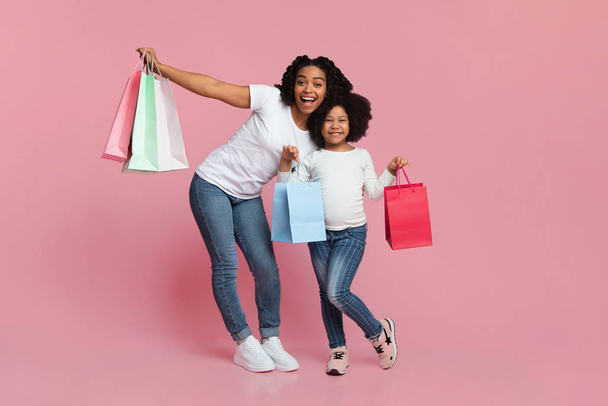 Glückliche schwarze Mutter und Tochter posieren mit Einkaufstaschen, rosa Hintergrund - Foto, Bild