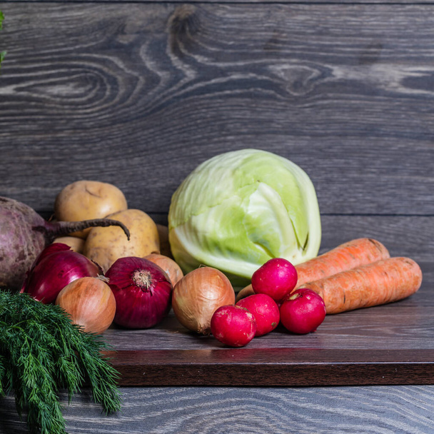 Different vegetables on a wooden table. Cabbage, potatoes, radishes, onions, carrots. - Photo, image
